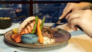 Hands cutting up food on a plate with a lobster tale and vegetables